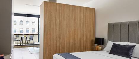 Une chambre d’hôtel moderne dotée d’un grand lit, d’une cloison en bois, d’une vue sur la ville et d’un balcon avec des sièges d’extérieur.