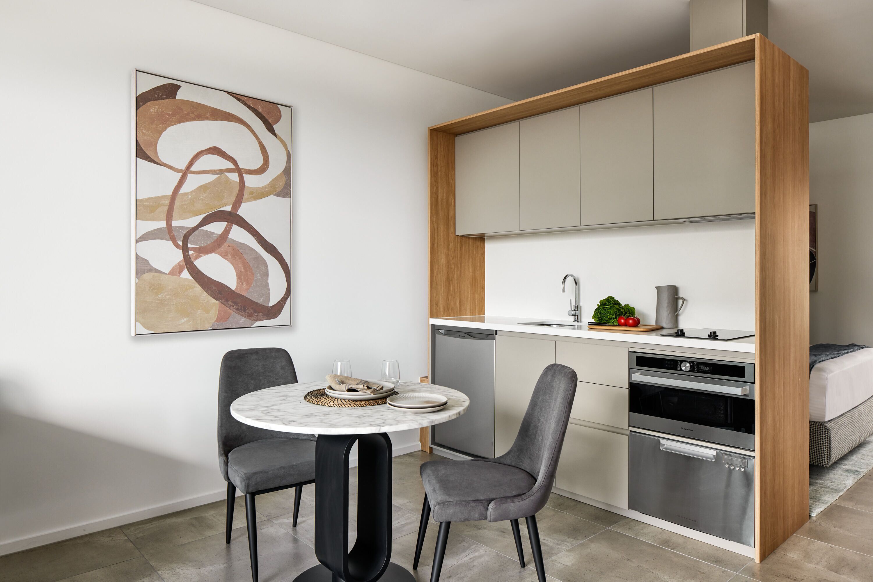 A compact kitchen with modern appliances, a dining area with a marble table, and a minimalist abstract painting on the wall.