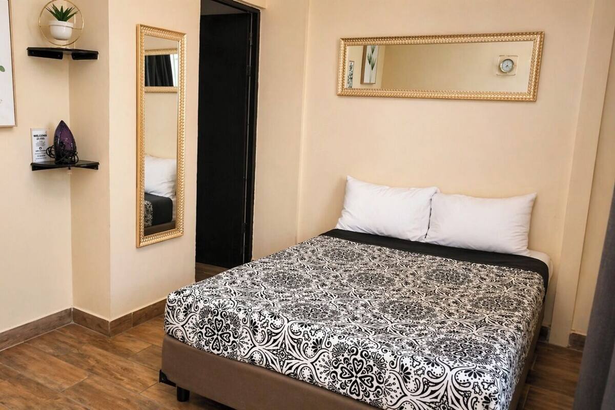 A bedroom with a bed, two mirrors, a potted plant, and a welcome sign.