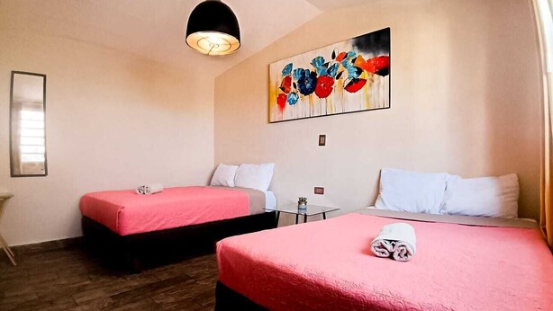Camera d'albergo con due letti, ognuno con copripiumino rosso e cuscini bianchi. Sopra i letti, un quadro appeso al muro; un tavolino con una pianta e una lampada a sospensione.