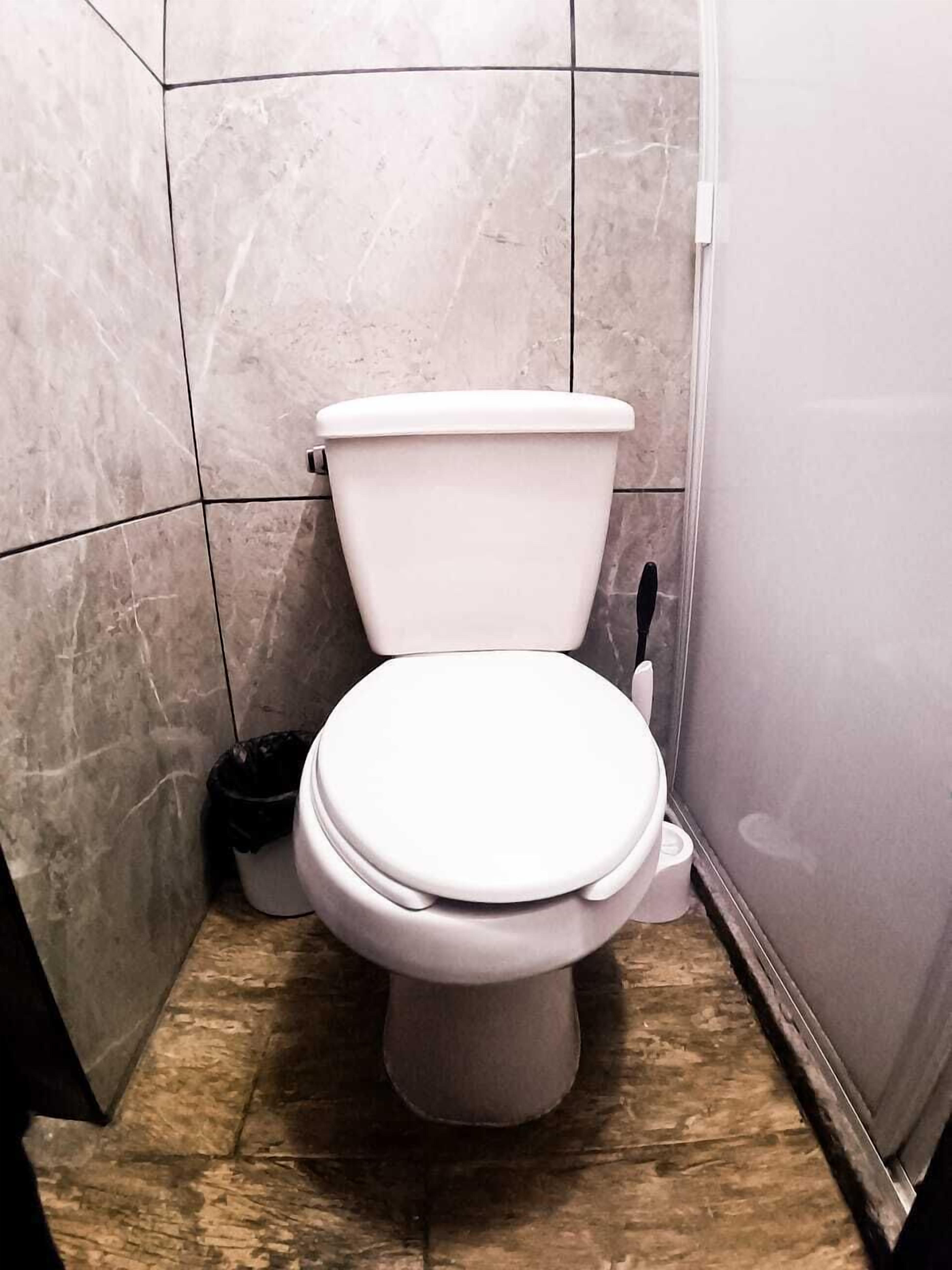 A toilet in a bathroom with tiled walls and a wooden floor.