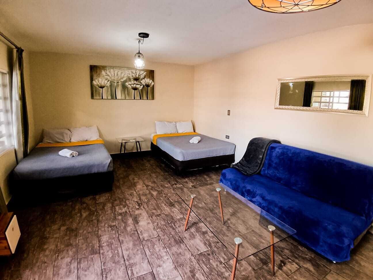 Una habitación con dos camas, un sofá azul, una mesita y un cuadro en la pared.