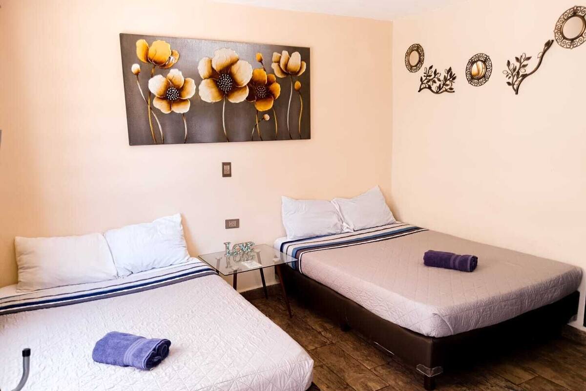 A room with two beds, a glass table, and a wall with a floral painting and decorative wall art.