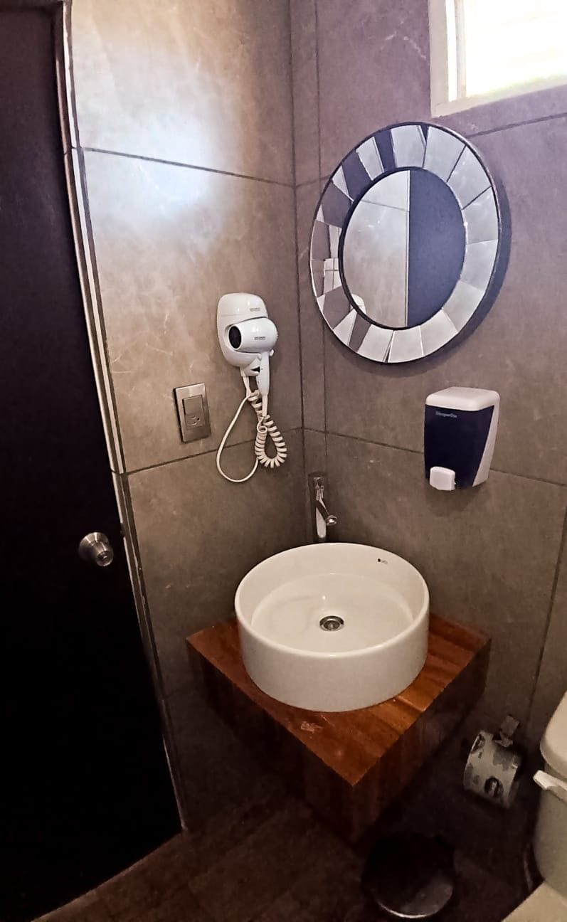A bathroom with a round mirror, a white sink, a handheld hair dryer, and a soap dispenser.