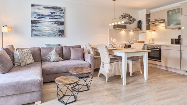 Un salon moderne comprenant un canapé, une table à manger et des chaises. On y trouve également un coin cuisine équipé d’appareils électroménagers et un luminaire suspendu.