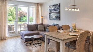 Un salon moderne avec un canapé, une table à manger et des chaises, de grandes fenêtres avec des rideaux et un tableau accroché au mur.