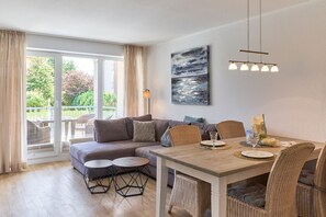 Una sala de estar moderna con un sofá, una mesa de comedor y sillas, ventanas grandes con cortinas y un cuadro en la pared.