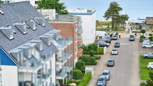 Une rue résidentielle bordée de voitures garées, offrant une vue dégagée sur le ciel, et un immeuble dont la façade présente un aspect texturé particulier.