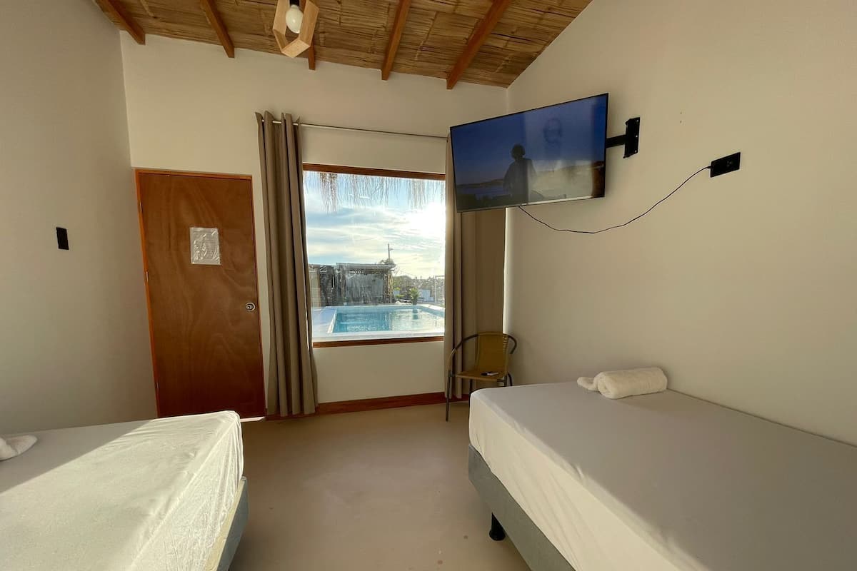 Ein Hotelzimmer mit zwei Betten, einem an der Wand montierten Fernseher, einem Fenster mit Blick auf einen Pool und ein Gebäude sowie einer Tür mit einem Schild.