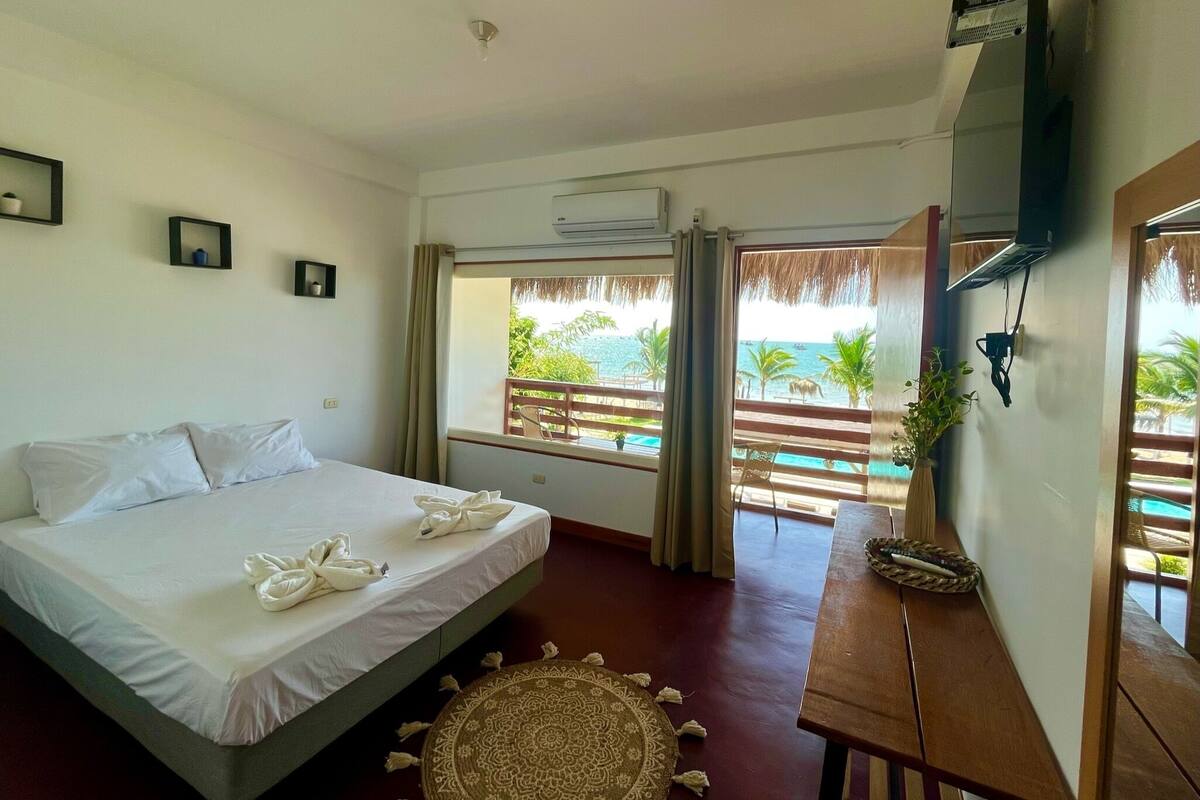 Ein Hotelzimmer mit Bett, Fernseher, Fenster mit Meerblick und einem Holztisch.