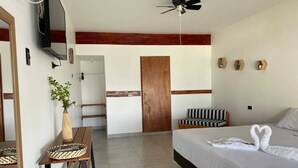 Una habitación de hotel con cama, escritorio, silla, televisor y ventilador de techo.