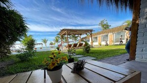 Un banco de madera con una planta en maceta y un adorno. Al fondo, se ve una zona de piscina con sillas de descanso y un área de estar cubierta.
