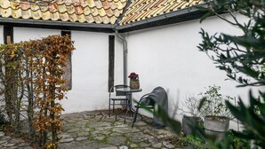 En gårdsplads med tegltag, en hvid mur, et lille bord med stol og plantede planter.