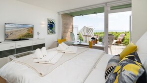 A hotel room with a bed, a desk with a chair, a television, and a balcony with chairs and a table.