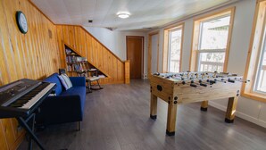 Et værelse med et bordtennisbord, en blå sofa, et keyboard og en bogreol.