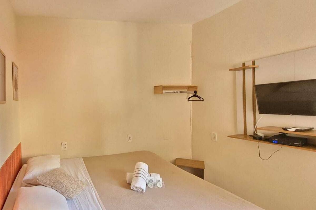 A hotel room with a bed, a TV, a shelf with a remote, and a towel on the bed.