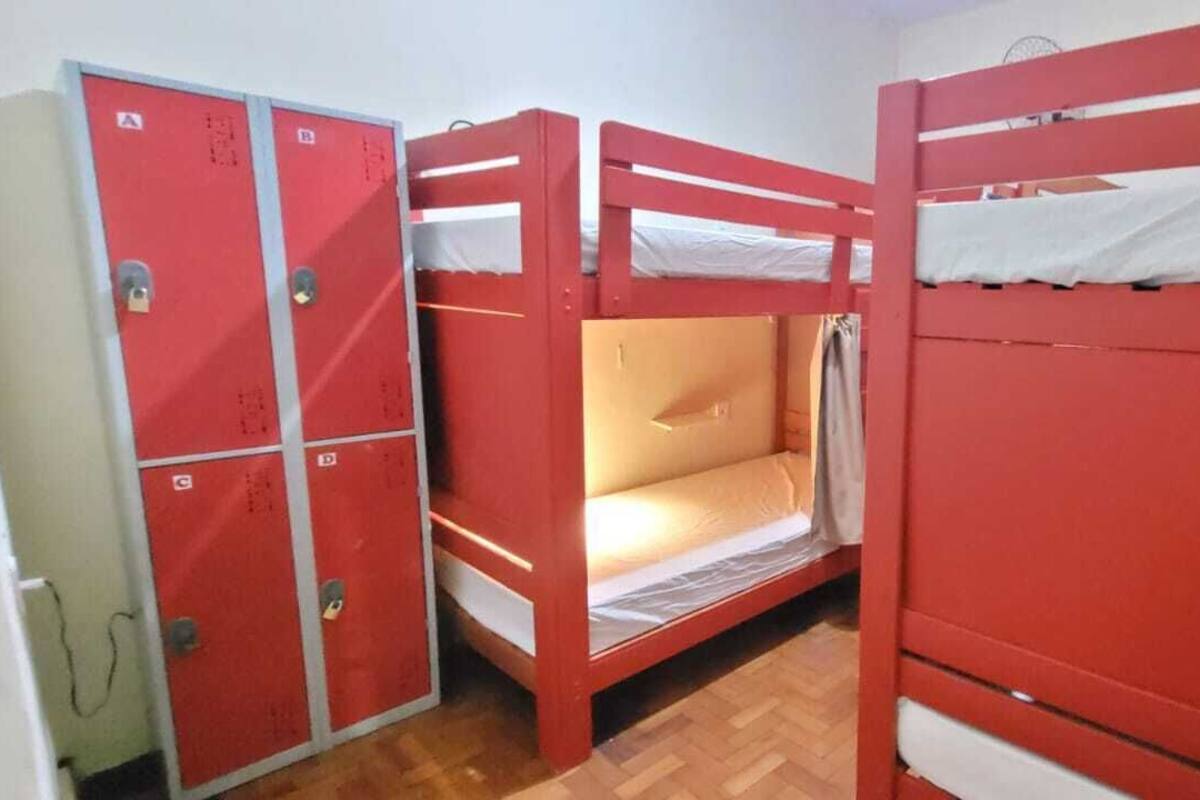 A dormitory room with bunk beds, a wardrobe, and a small window.