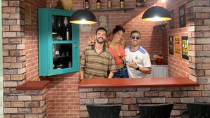 Zona de bar con paredes de ladrillo, armarios color turquesa, lámparas colgantes negras y una barra.