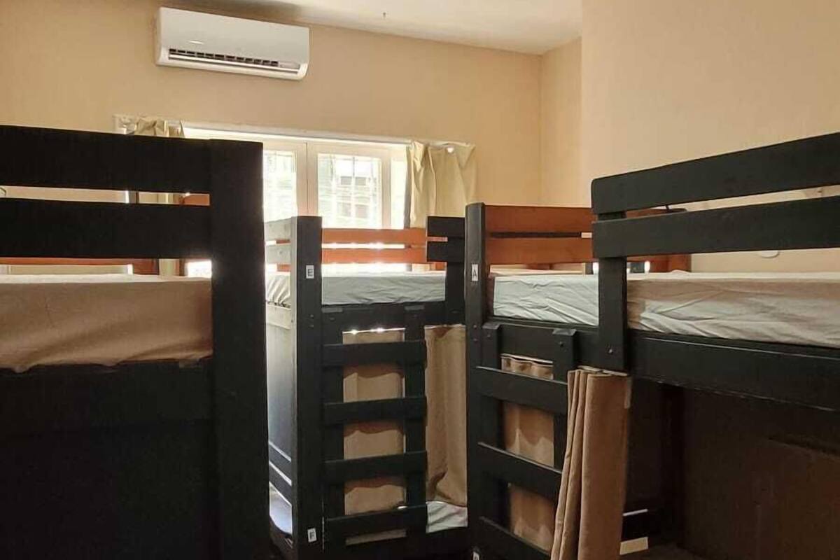 A dormitory room with bunk beds, a ceiling fan, and a window with curtains.