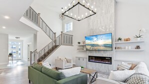 Un salon spacieux avec un canapé vert, une cheminée, un téléviseur fixé au mur et un escalier.