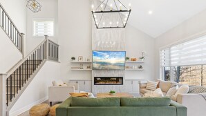 Un salon moderne avec un canapé vert, une cheminée, un escalier et une grande fenêtre.