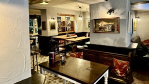 A restaurant with a wooden table and chairs, a menu stand, and a wall-mounted painting. - the black swan (Leyburn)