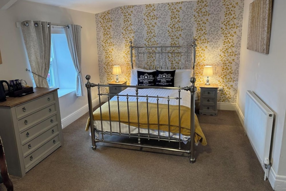 A bedroom with a four-poster bed, two bedside tables, a dresser, and a radiator.