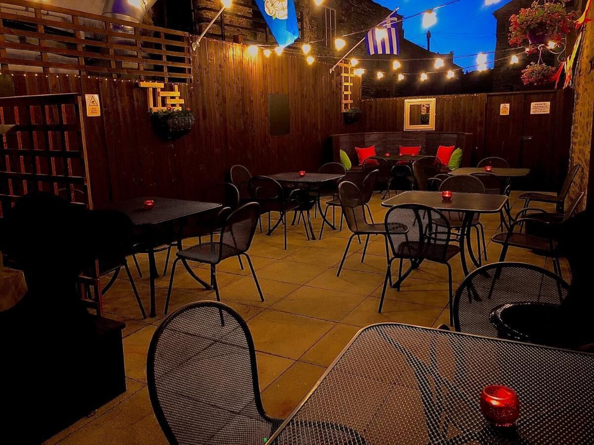 An outdoor dining area with tables and chairs, string lights, and a wooden fence.