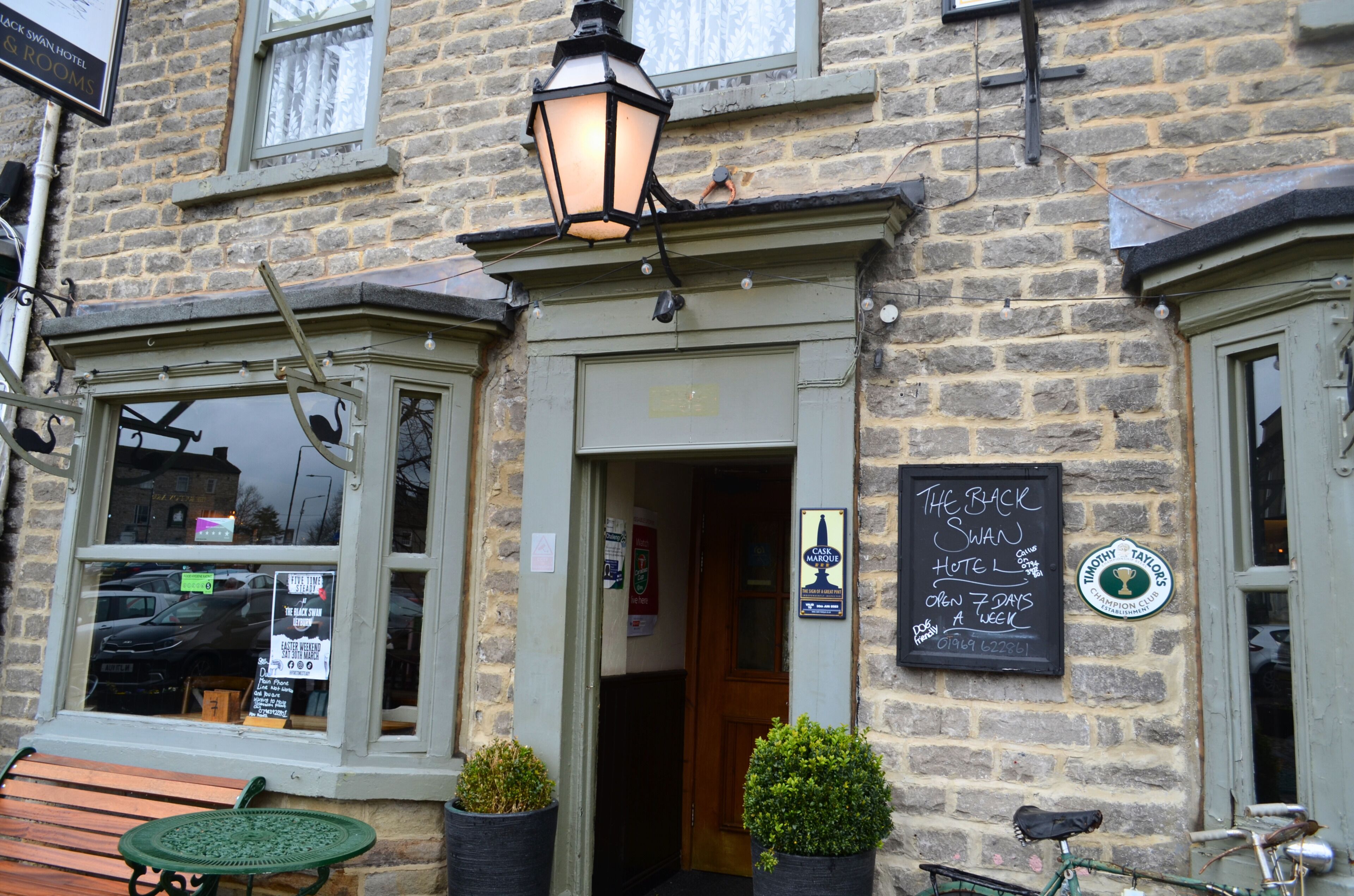 A stone building with a sign for The Back Swan Hotel, a wooden bench, and a bicycle.