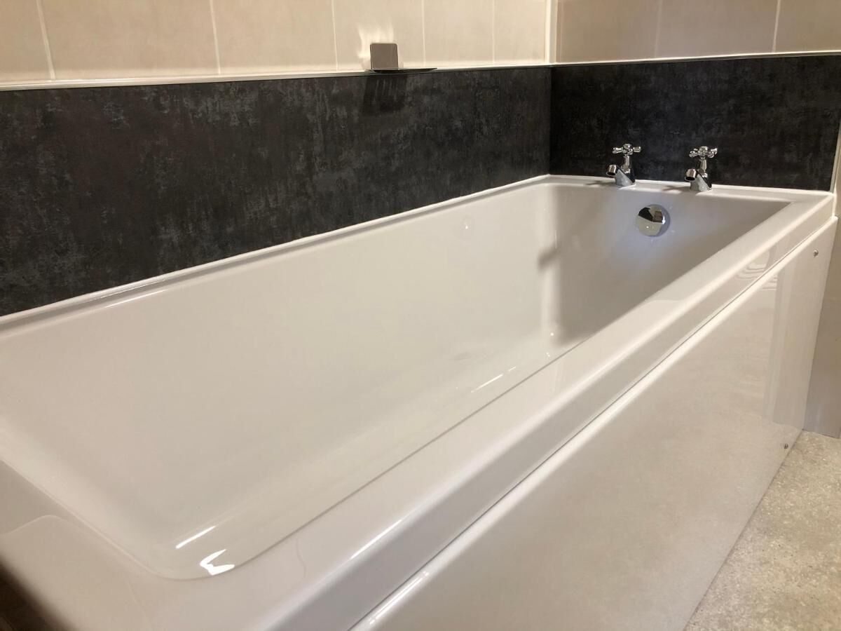 A modern bathroom with a large white bathtub, dark tiled walls, and a small shelf above the tub.