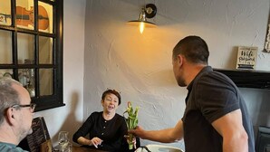 A group of people seated around a wooden table in a room with a textured wall and a hanging light fixture. - the black swan (Leyburn)