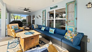 Une pièce lumineuse, avec un canapé bleu, des fauteuils en osier, une table basse en bois et un ventilateur de plafond.