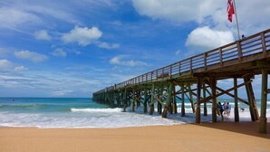 Une jetée en bois s’étendant dans l’océan, avec une plage de sable au premier plan.