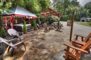 An outdoor patio with stone flooring, wooden chairs, a hot tub, and string lights. - BEAUTIFUL PREMIER CABIN!!! 2 bedroom NEWLY RENOVATED CABIN WITH HOT TUB!!! (Helen)