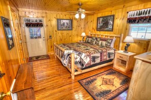 A wooden cabin bedroom with a bed, a nightstand, a lamp, a ceiling fan, and a window. - BEAUTIFUL PREMIER CABIN!!! 2 bedroom NEWLY RENOVATED CABIN WITH HOT TUB!!! (Helen)
