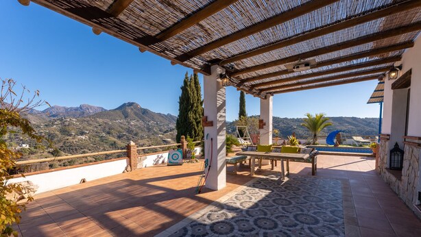 Un pati exterior cobert amb un paviment estampat, una taula i caires, i vista a les muntanyes.