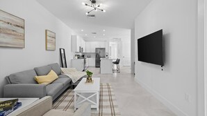 A modern living room with a gray sofa, a coffee table, and a TV mounted on the wall. - NAPLES GEM (Naples)