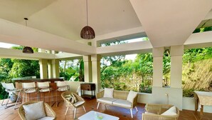Un vaste patio doté d’un bar, de meubles en osier et offrant une vue sur une végétation luxuriante.