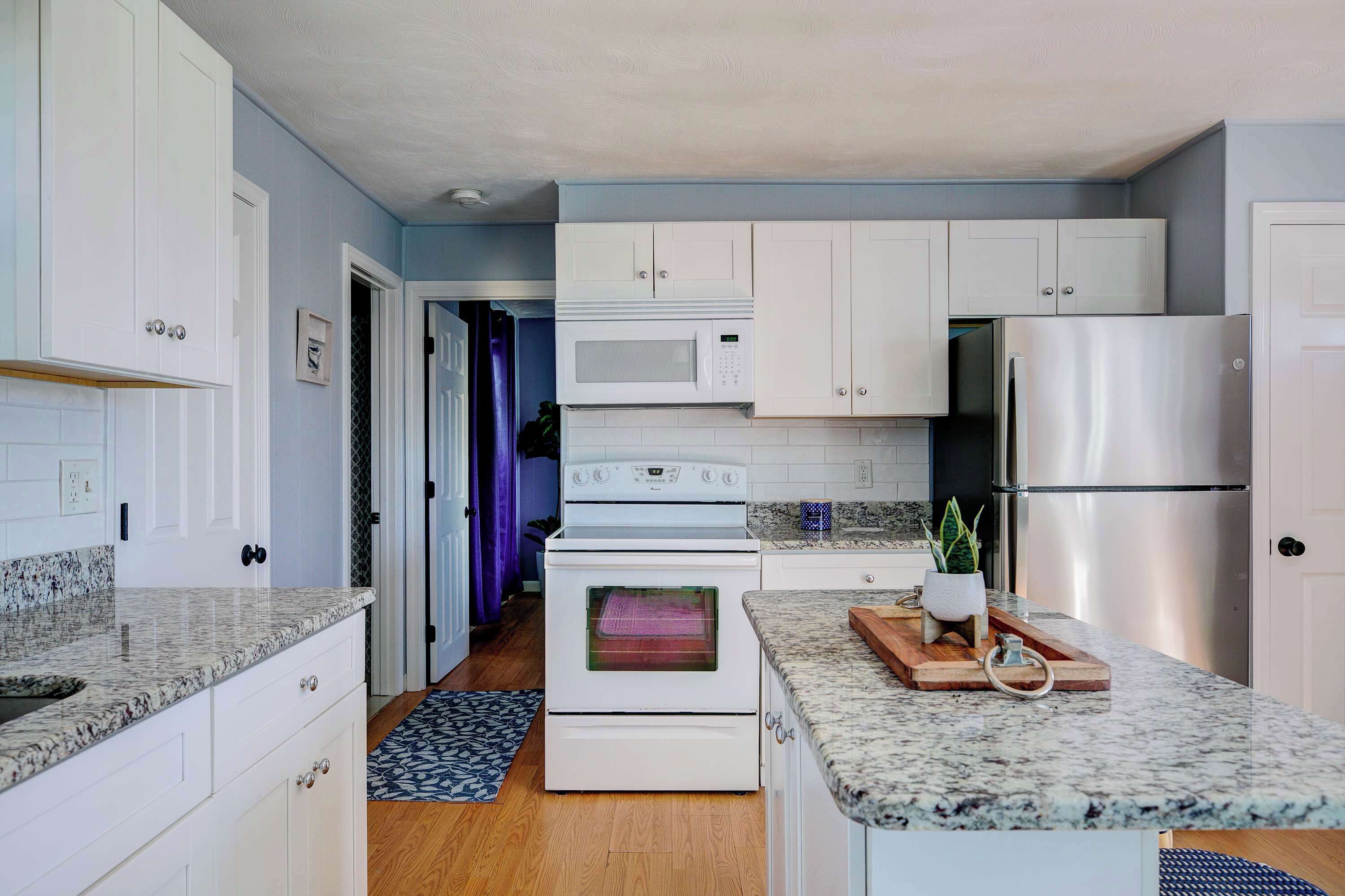 A kitchen with white cabinets, a microwave, a stainless steel refrigerator, and granite countertops.