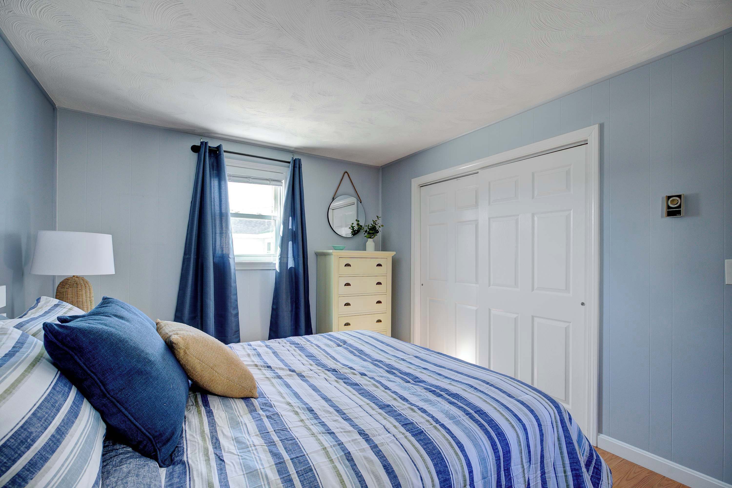 Quarto com cama, cômoda, espelho e porta.