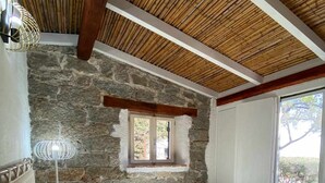 Une chambre avec un mur en pierre, un plafond en bois, un lit avec une literie à motifs, une fenêtre et une lampe de sol.