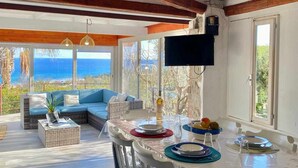 Une salle à manger spacieuse, dotée d’une grande table, de chaises blanches et offrant une vue sur la mer grâce à de larges fenêtres.