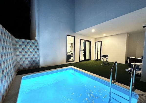A swimming pool with a ladder, a door leading to a room, and a patterned wall.