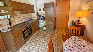 A compact kitchen with wooden cabinets, a stove, and a dining area with a table and chairs.