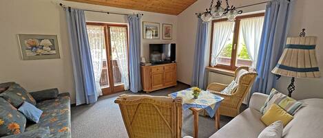 Een gezellige woonkamer met een houten plafond, een televisie, een eettafel met stoelen en een bank.