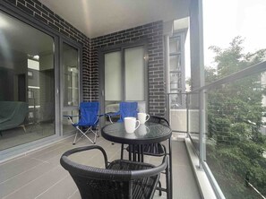 Enjoy a peaceful moment on this balcony with a round table and two comfortable chairs, overlooking a serene green space with trees.