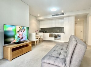 Relax in this stylish living space featuring a flat-screen TV, tufted sofa, and dining area with a white table and chairs.