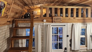 Interior de una cabaña con techo de madera, un altillo, una escalera, una puerta y un letrero que dice 'THE CABIN IS MY HAPPY PLACE'.
