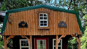 Una cabaña de madera con puerta roja, un porche delantero y una pequeña terraza.