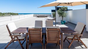 A rooftop terrace with a table and chairs, a large umbrella, and a view of the sea. - Penthouse with private solarium and pool sea views (L'Ametlla de Mar)